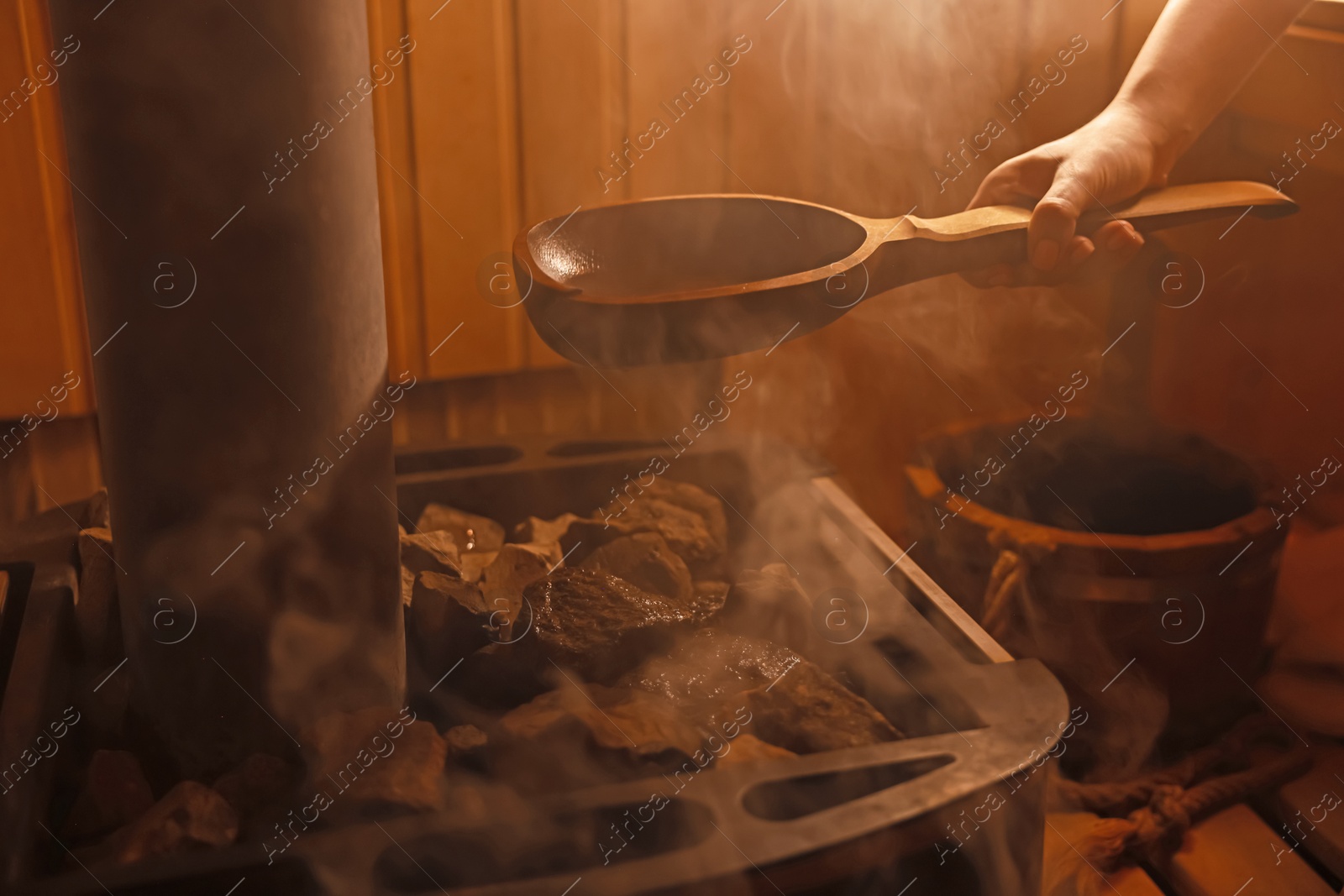 Photo of Woman pouring water on stones in sauna, closeup