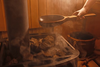 Photo of Woman pouring water on stones in sauna, closeup