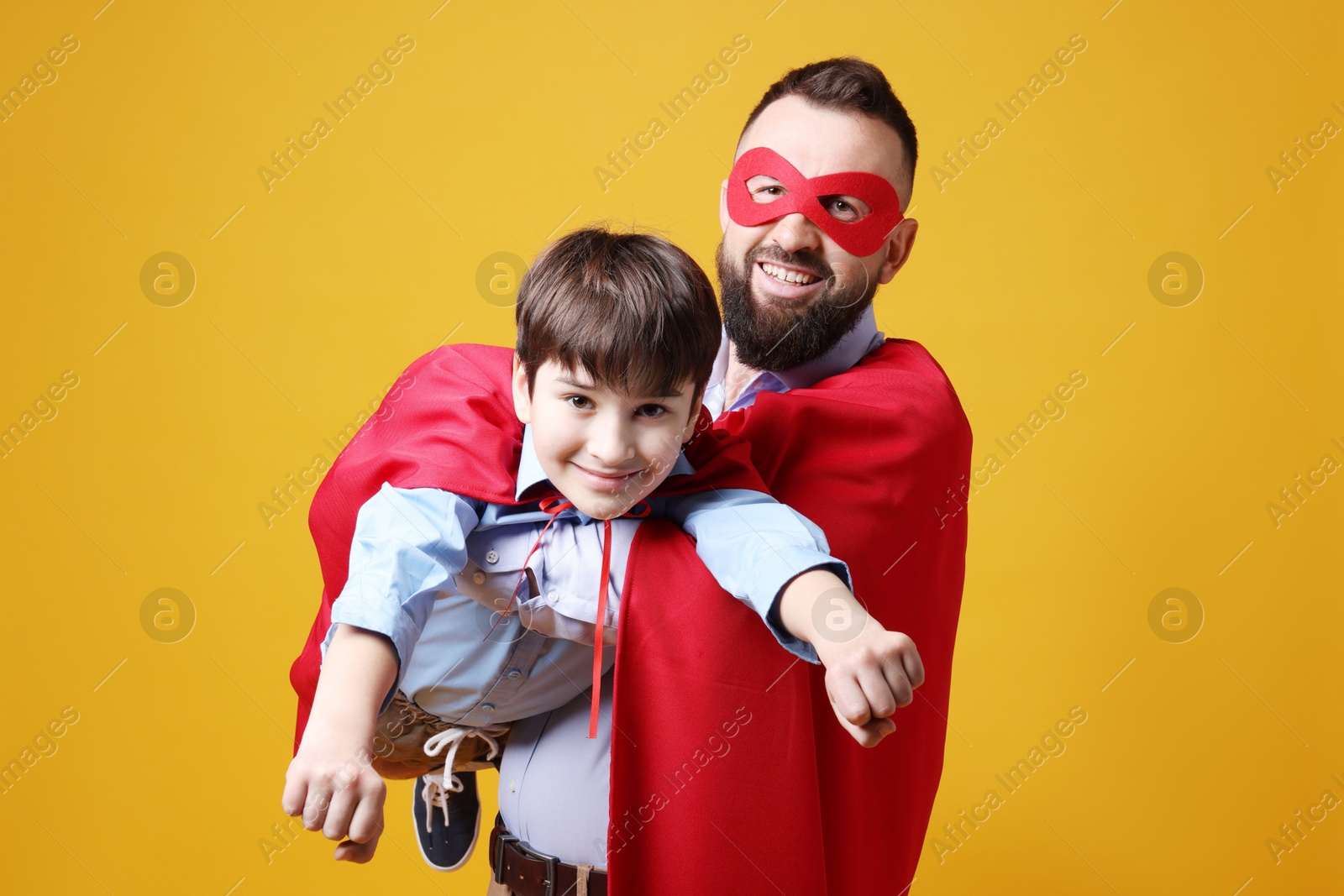 Photo of Father and his son wearing superhero costumes on orange background