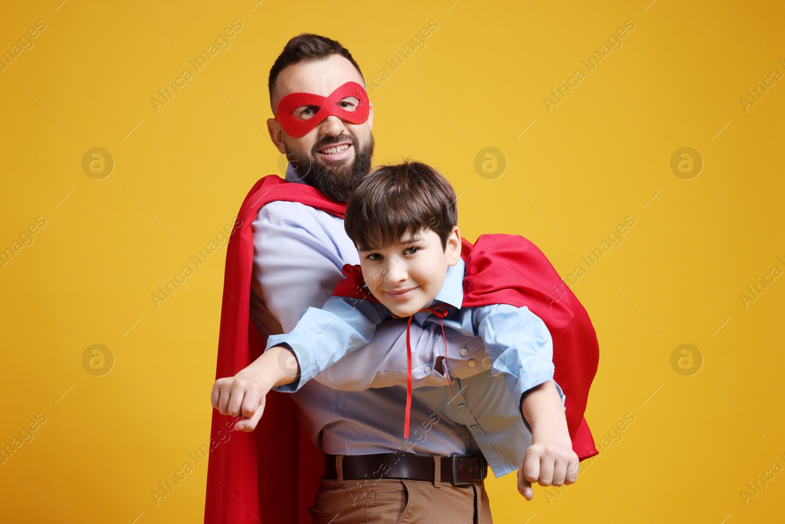 Photo of Father and his son wearing superhero costumes on orange background