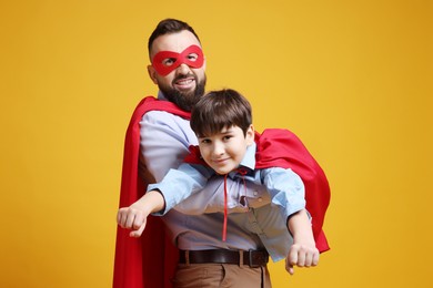 Father and his son wearing superhero costumes on orange background