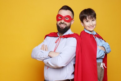 Father and his son wearing superhero costumes on orange background, space for text