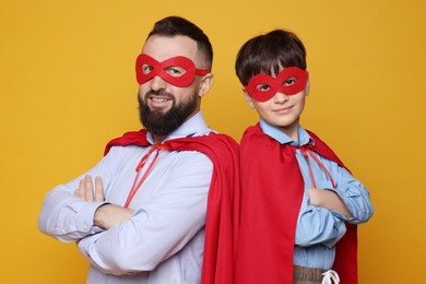 Photo of Father and his son wearing superhero costumes on orange background