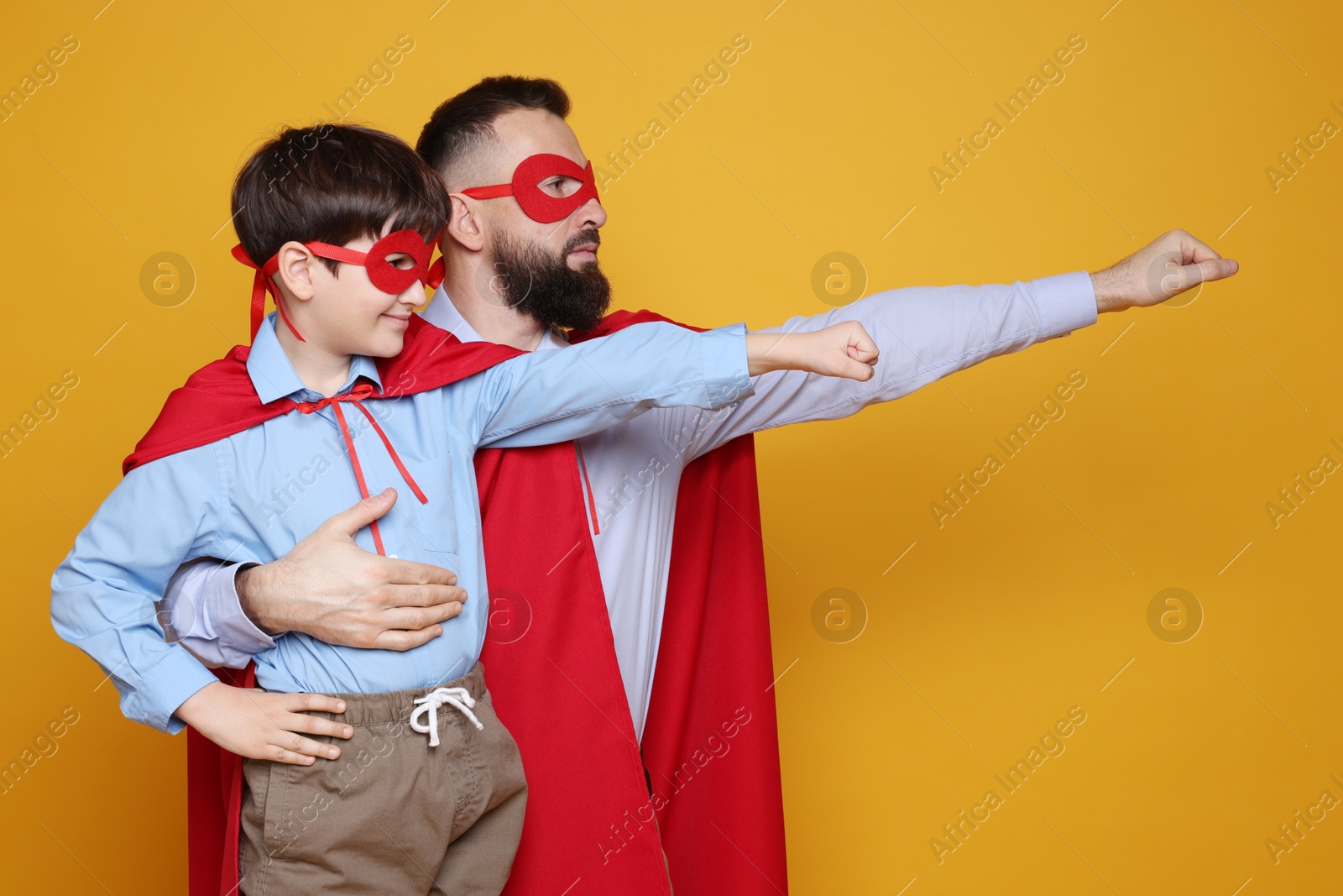 Photo of Father and his son wearing superhero costumes on orange background