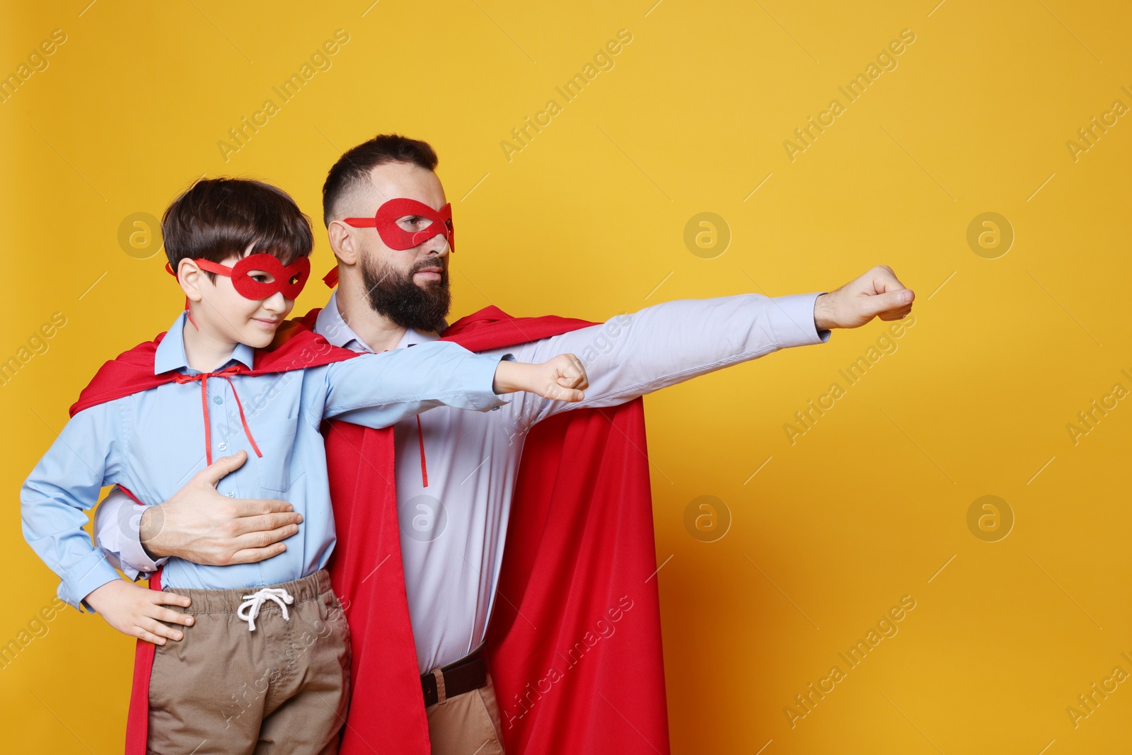 Photo of Father and his son wearing superhero costumes on orange background