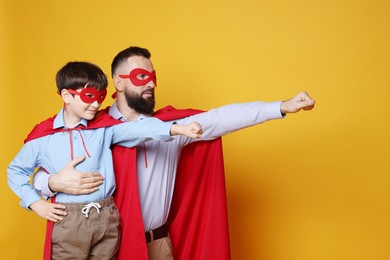 Father and his son wearing superhero costumes on orange background