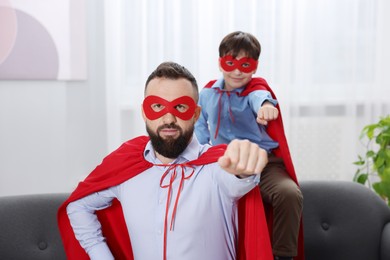 Photo of Father and his son wearing superhero costumes at home, selective focus