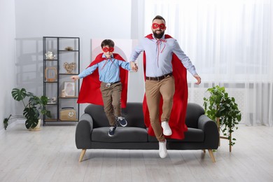 Father and his son in superhero costumes jumping at home