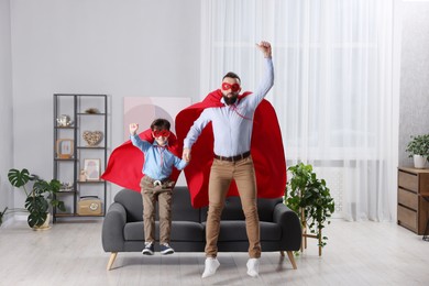 Photo of Father and his son in superhero costumes jumping at home