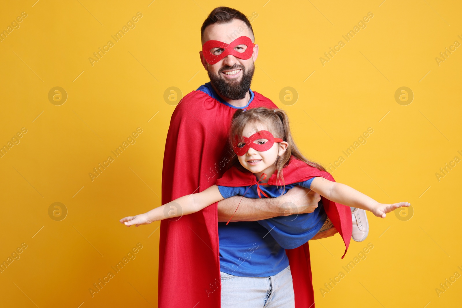 Photo of Father and his cute little daughter wearing superhero costumes on orange background