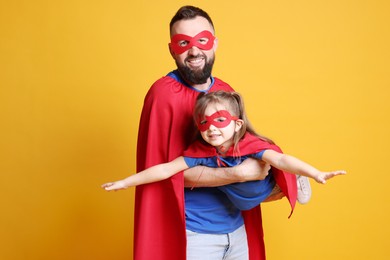 Photo of Father and his cute little daughter wearing superhero costumes on orange background