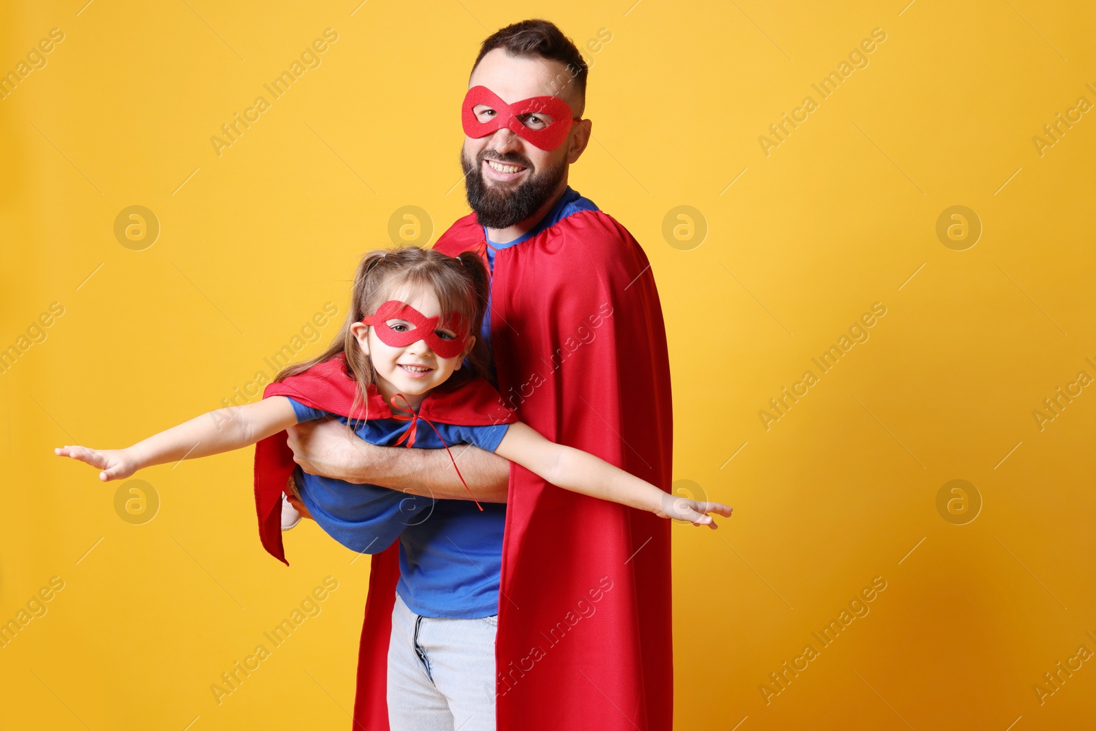 Photo of Father and his cute little daughter wearing superhero costumes on orange background