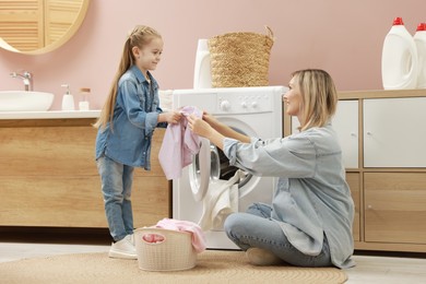 Photo of Mother and daughter with laundry basket loading washing machine together at home