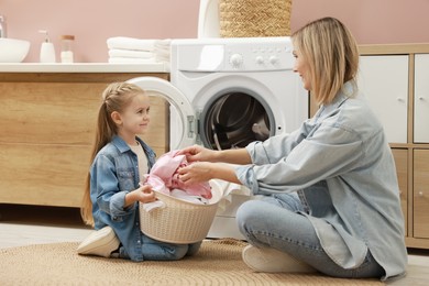 Photo of Mother and daughter with laundry basket loading washing machine together at home