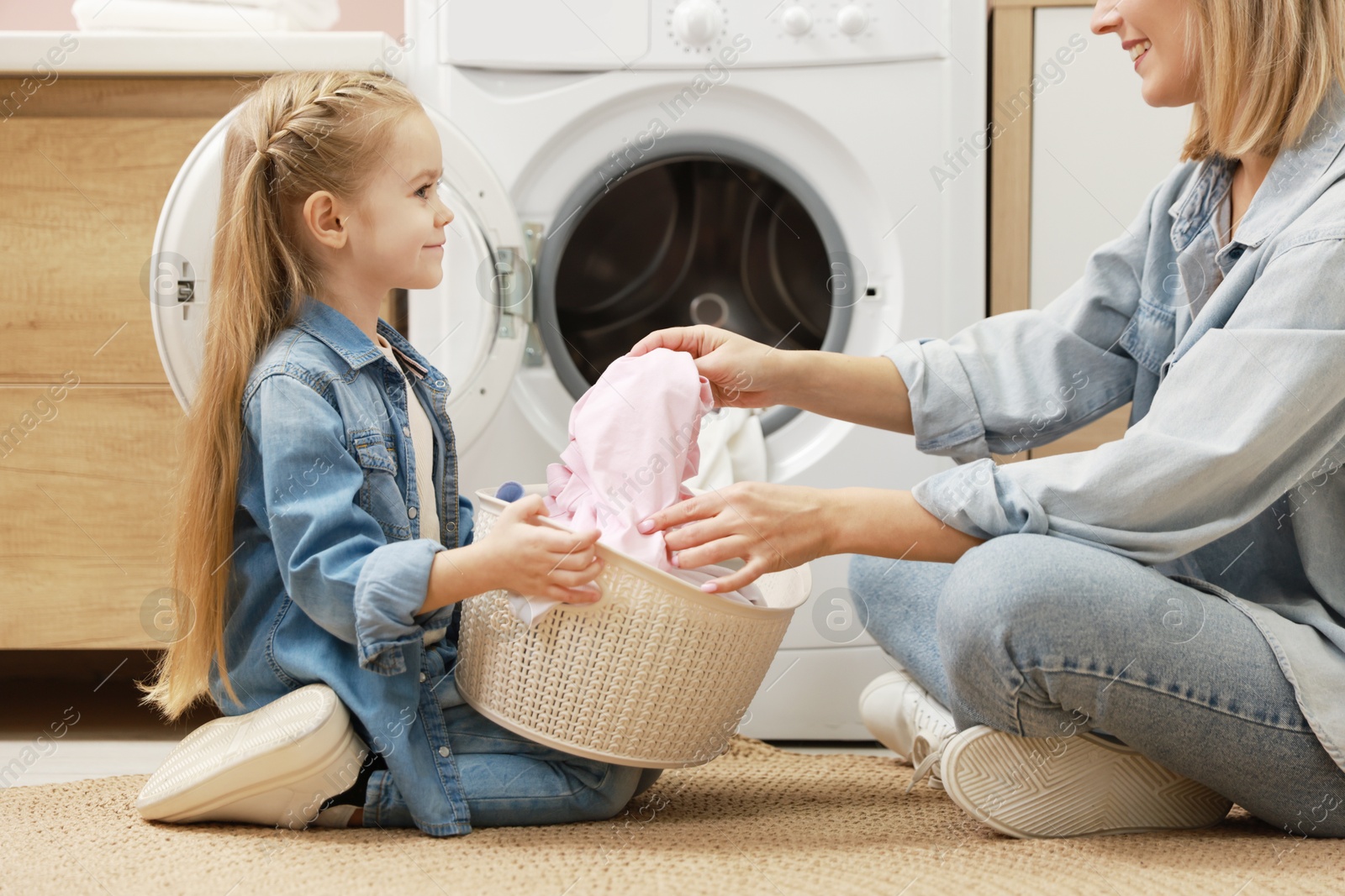 Photo of Mother and daughter with laundry basket loading washing machine together at home