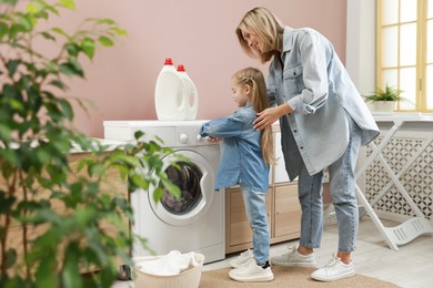 Photo of Little girl and her mom doing laundry together at home