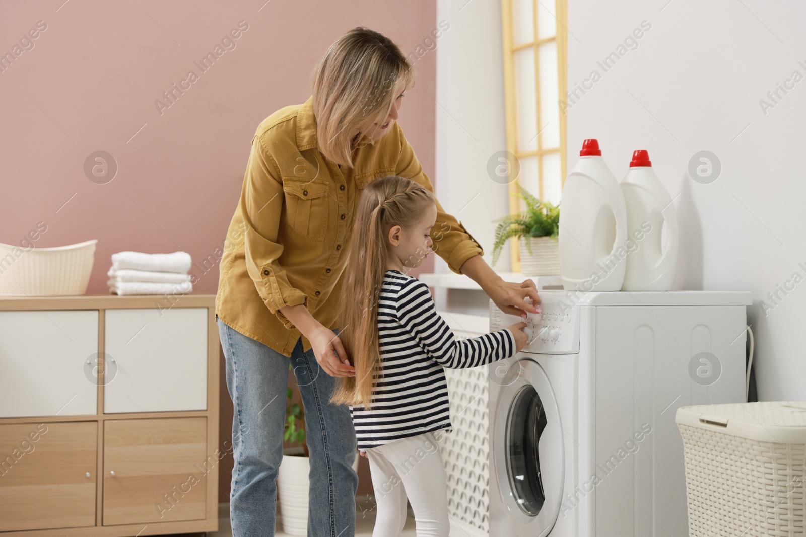 Photo of Little girl and her mom doing laundry together at home