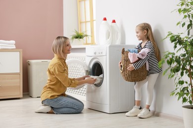 Photo of Little girl and her mom doing laundry together at home