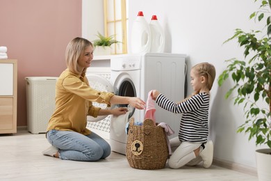 Photo of Little girl and her mom doing laundry together at home