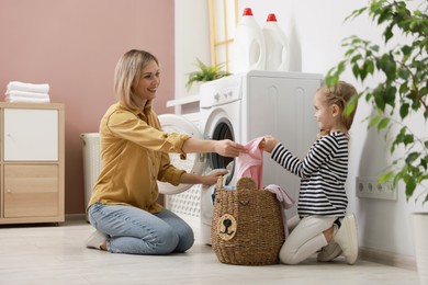 Photo of Little girl and her mom doing laundry together at home