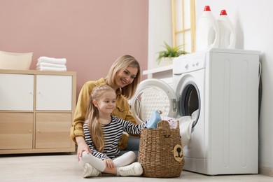 Mother and daughter with laundry basket loading washing machine together at home