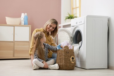 Photo of Mother and daughter with laundry basket loading washing machine together at home