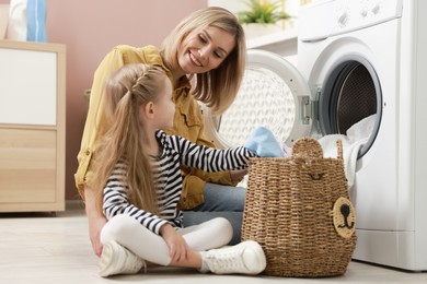 Photo of Mother and daughter with laundry basket loading washing machine together at home