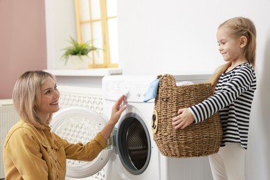 Photo of Little girl and her mom doing laundry together at home