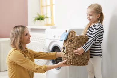 Photo of Little girl and her mom doing laundry together at home