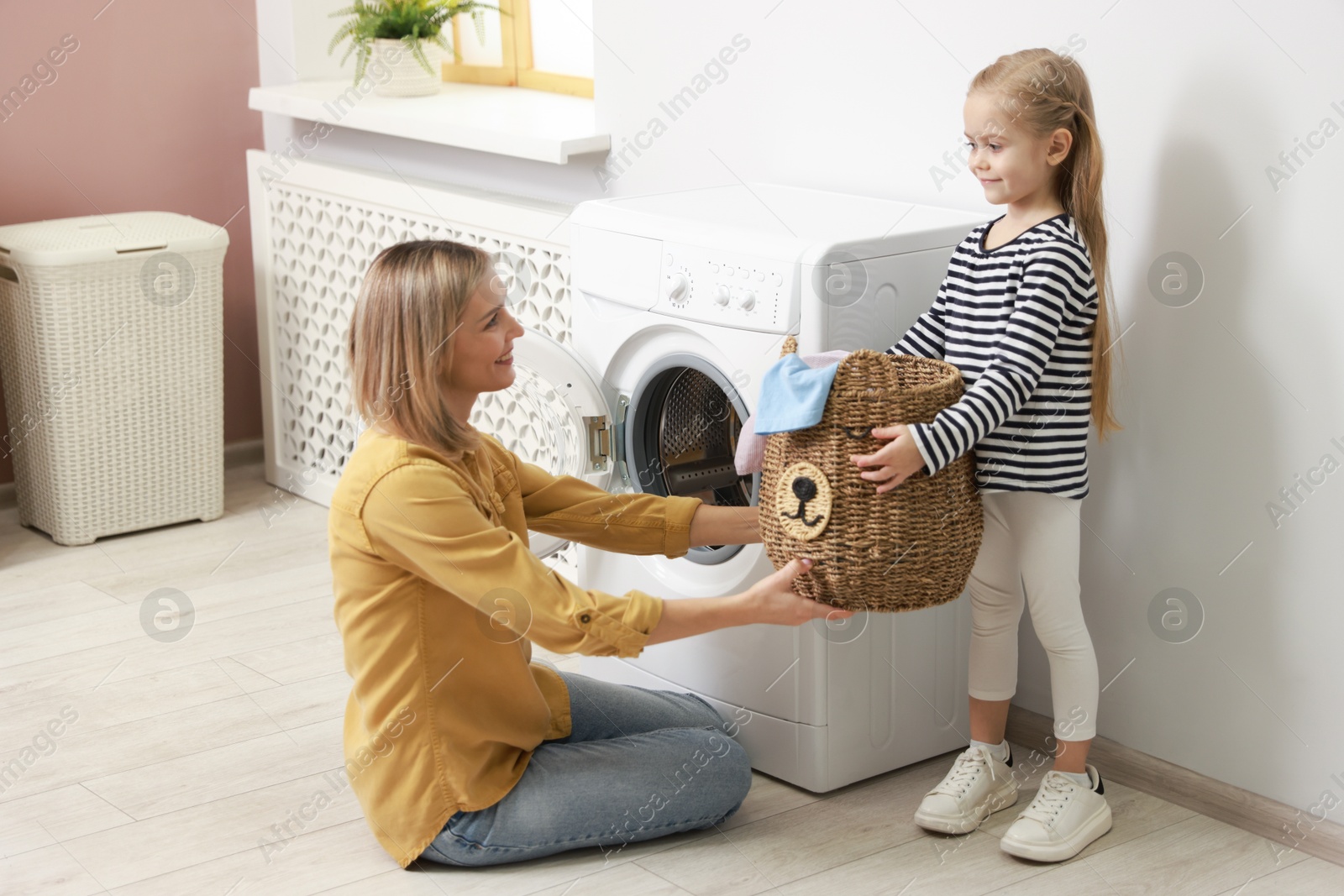 Photo of Little girl and her mom doing laundry together at home