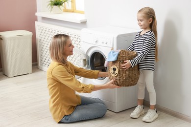 Photo of Little girl and her mom doing laundry together at home