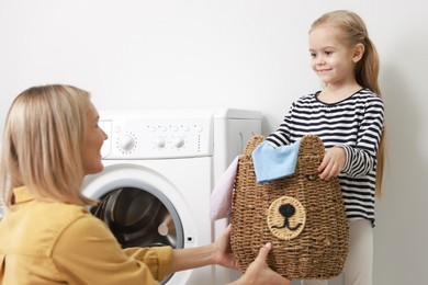 Photo of Little girl and her mom doing laundry together at home