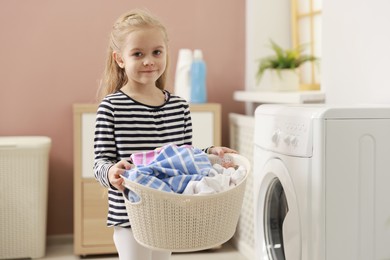 Photo of Cute little girl with laundry basket at home