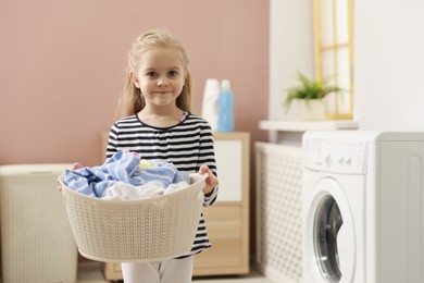 Photo of Cute little girl with laundry basket at home