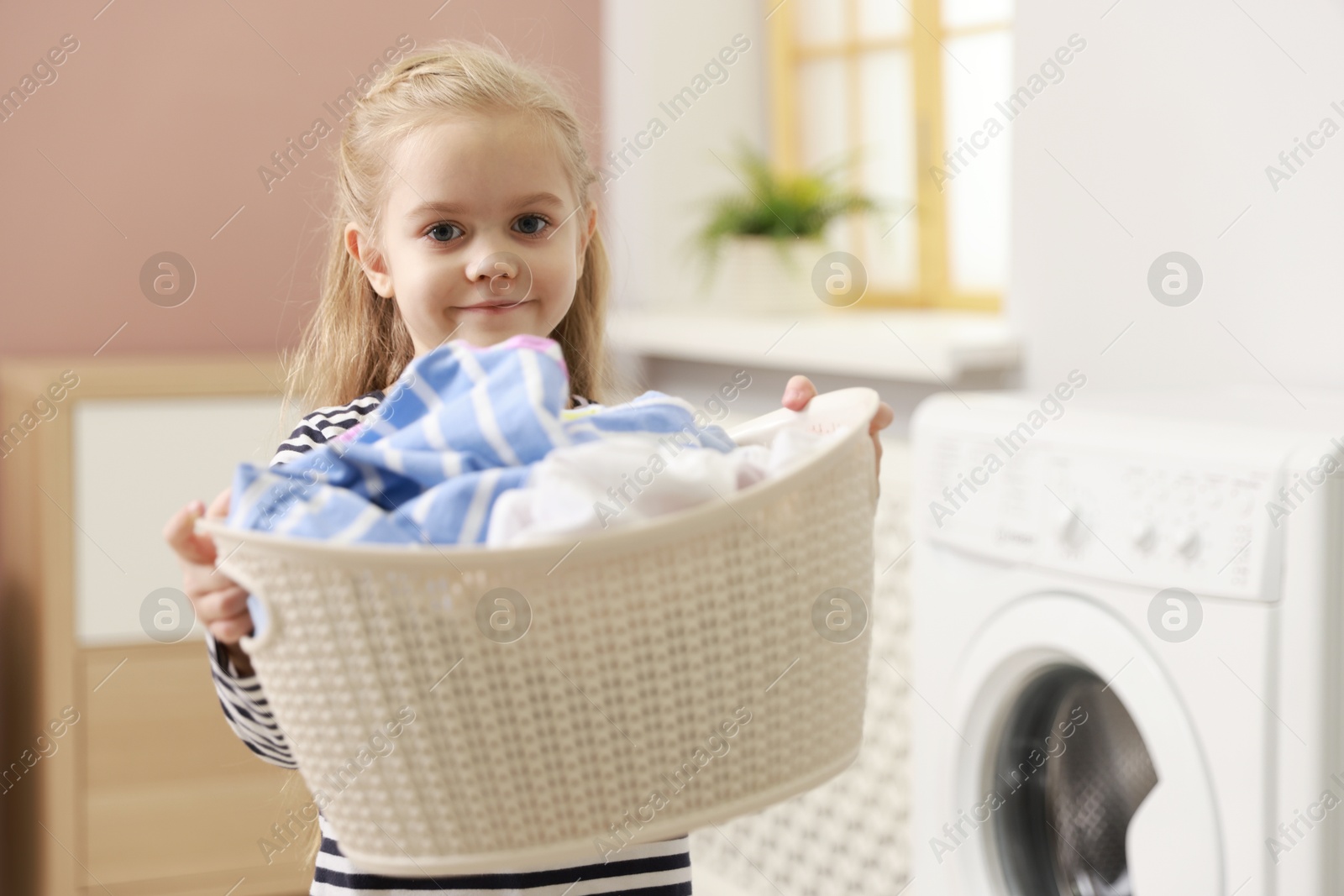 Photo of Cute little girl with laundry basket at home