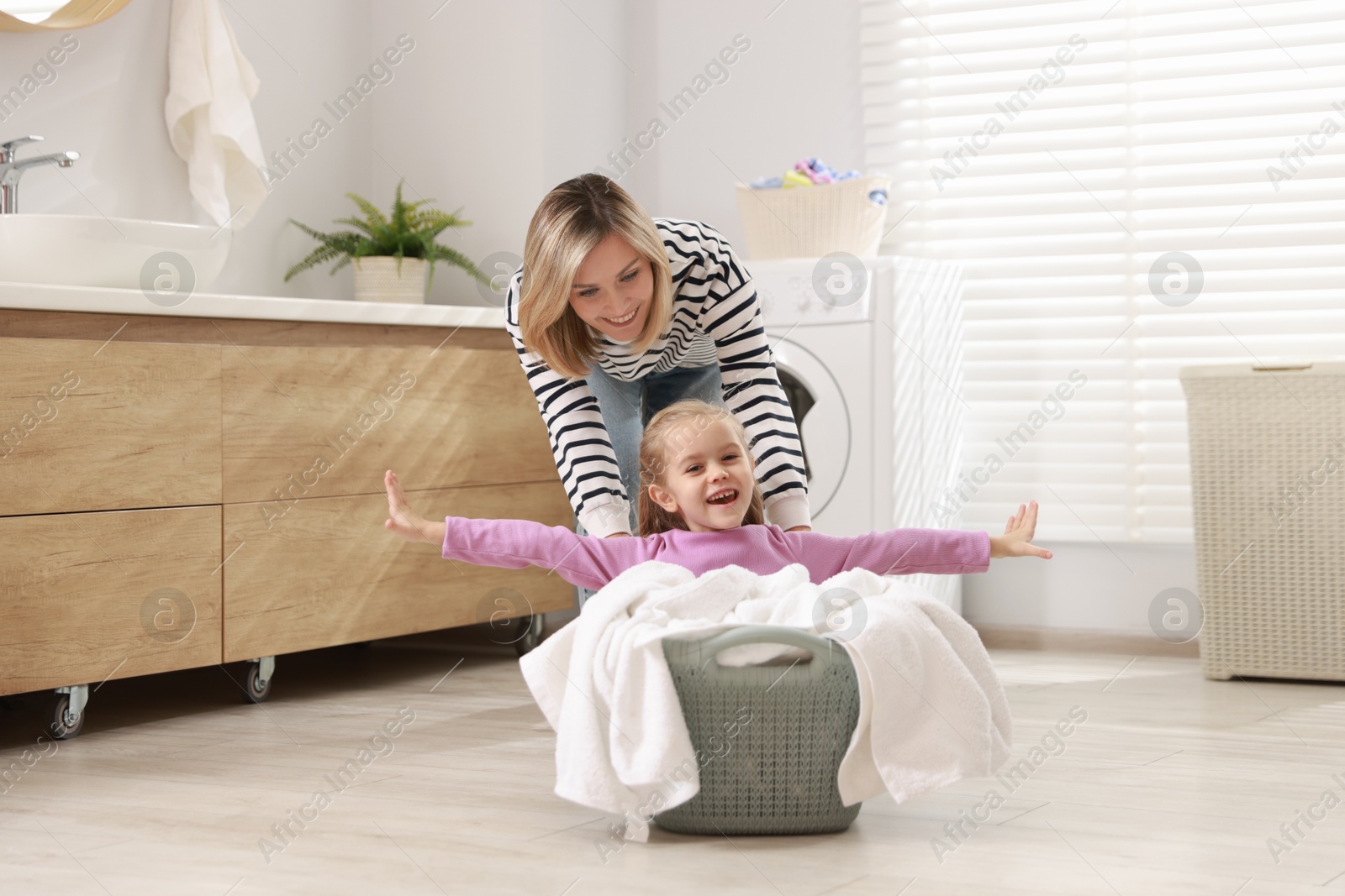 Photo of Mother and daughter having fun while doing laundry together at home