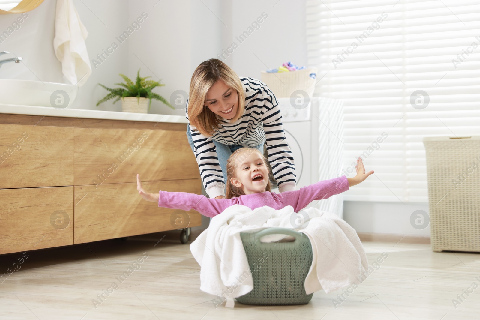 Photo of Mother and daughter having fun while doing laundry together at home