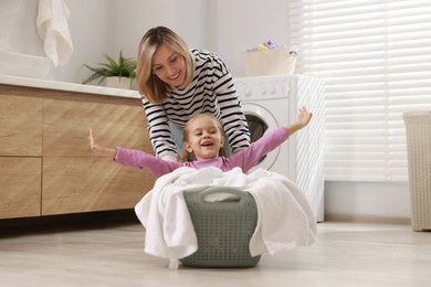 Mother and daughter having fun while doing laundry together at home