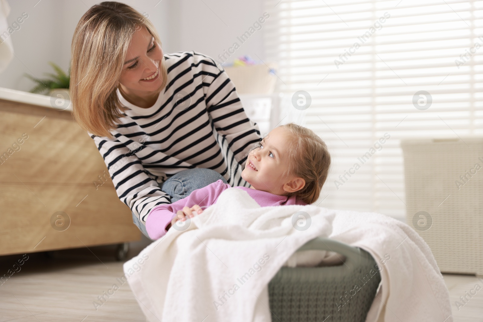 Photo of Mother and daughter having fun while doing laundry together at home