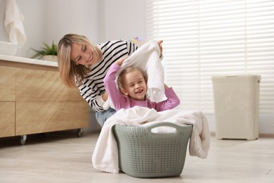 Mother and daughter having fun while doing laundry together at home