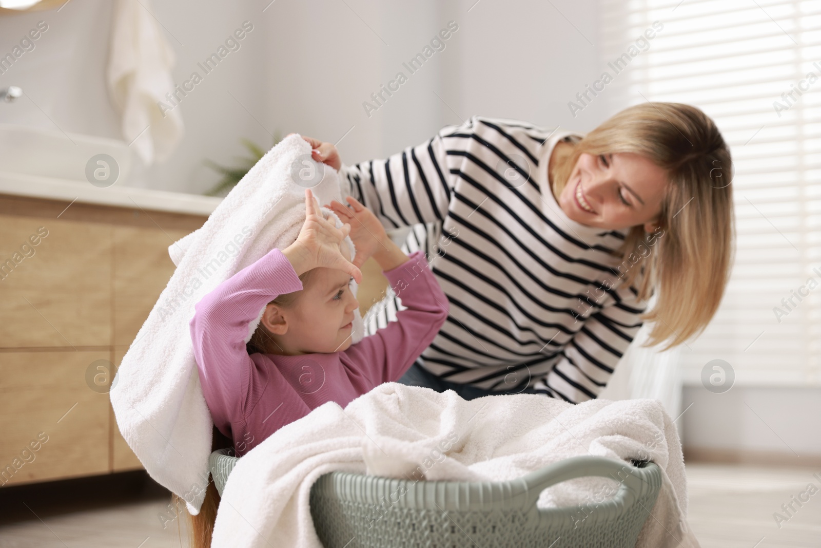 Photo of Little girl and her mom doing laundry together at home