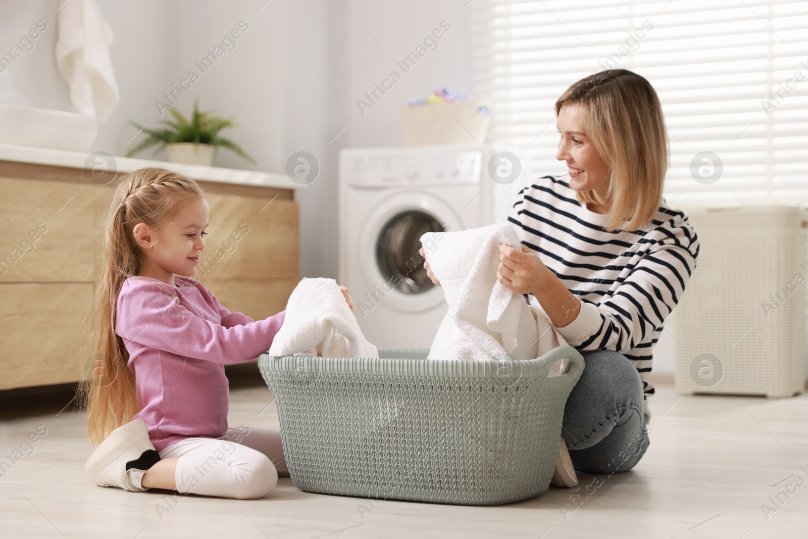 Photo of Little girl and her mom doing laundry together at home