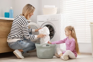 Photo of Mother and daughter with laundry basket loading washing machine together at home