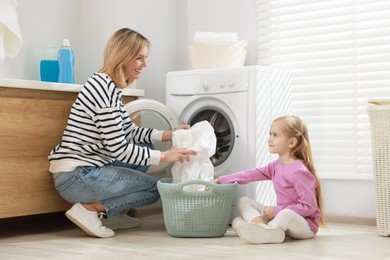 Photo of Mother and daughter with laundry basket loading washing machine together at home