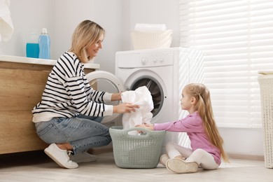 Photo of Mother and daughter with laundry basket loading washing machine together at home