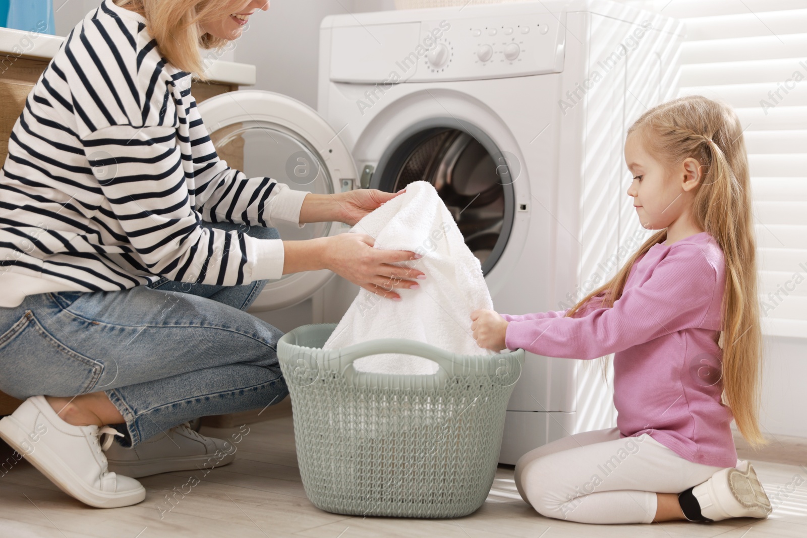 Photo of Mother and daughter with laundry basket loading washing machine together at home