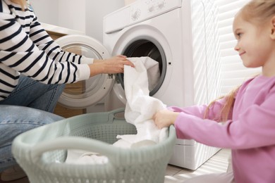 Photo of Mother and daughter with laundry basket loading washing machine together at home