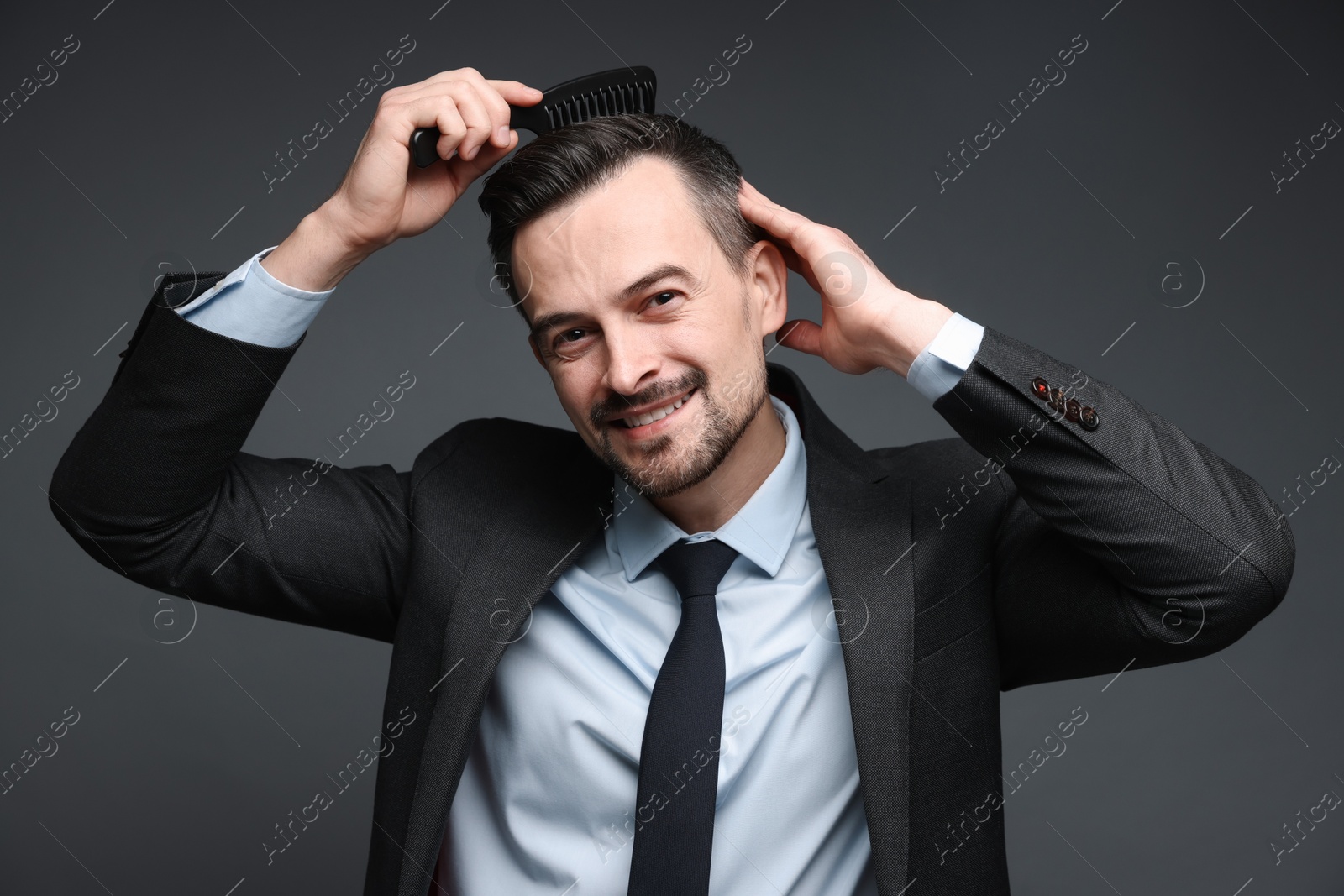 Photo of Handsome businessman combing his hair on dark background