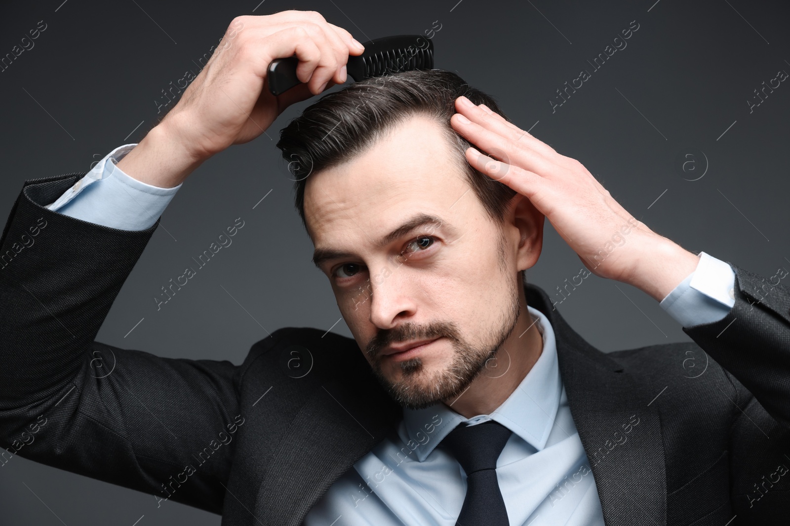 Photo of Handsome businessman combing his hair on dark background