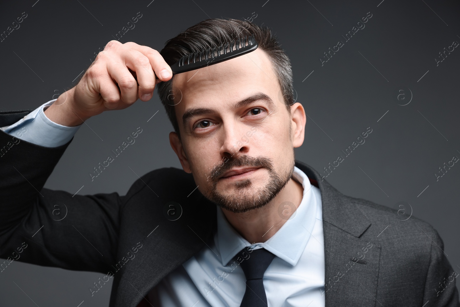 Photo of Handsome businessman combing his hair on dark background